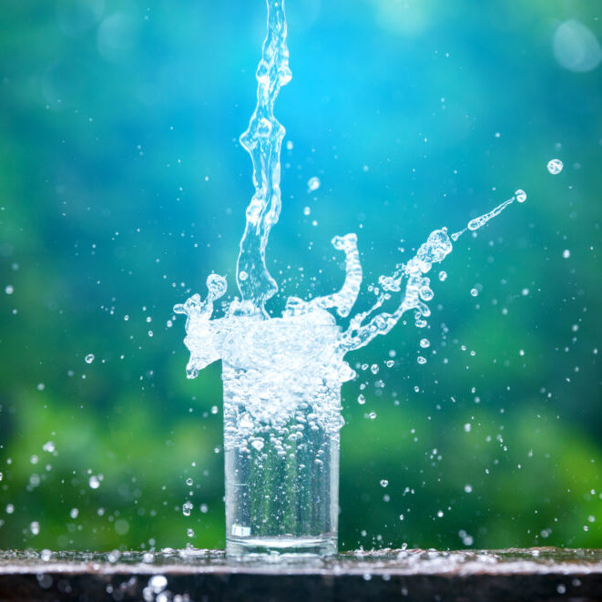 Drink water pouring in to glass over sunlight and natural green